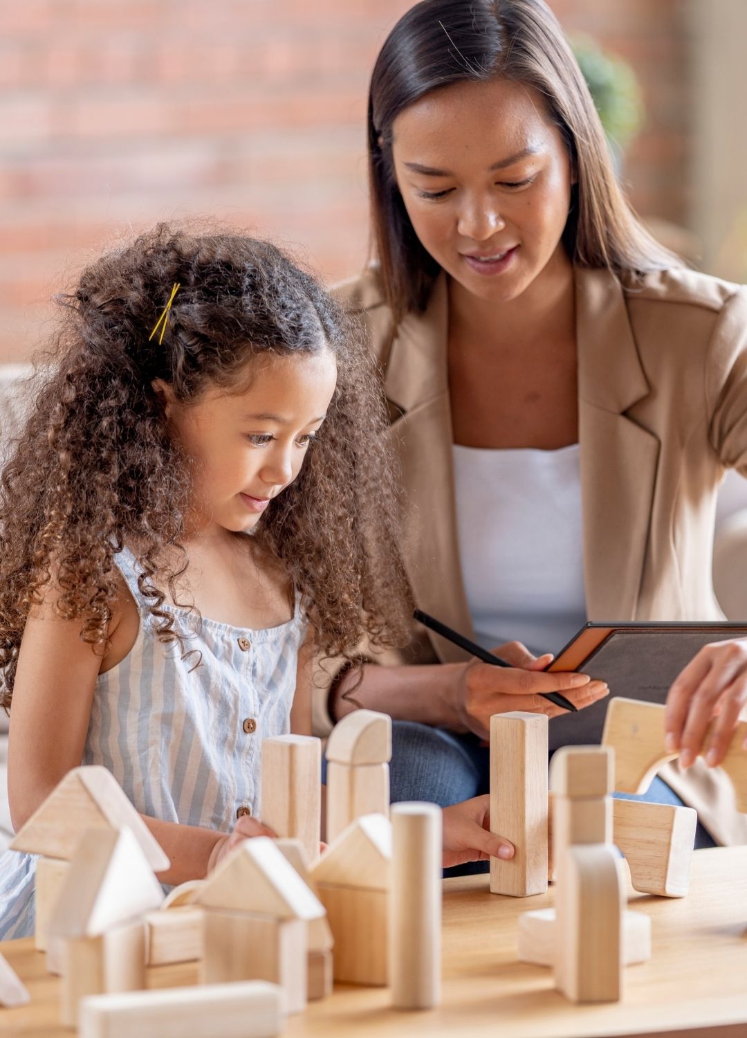 An adult and a child sit at a table building structures with wooden blocks.